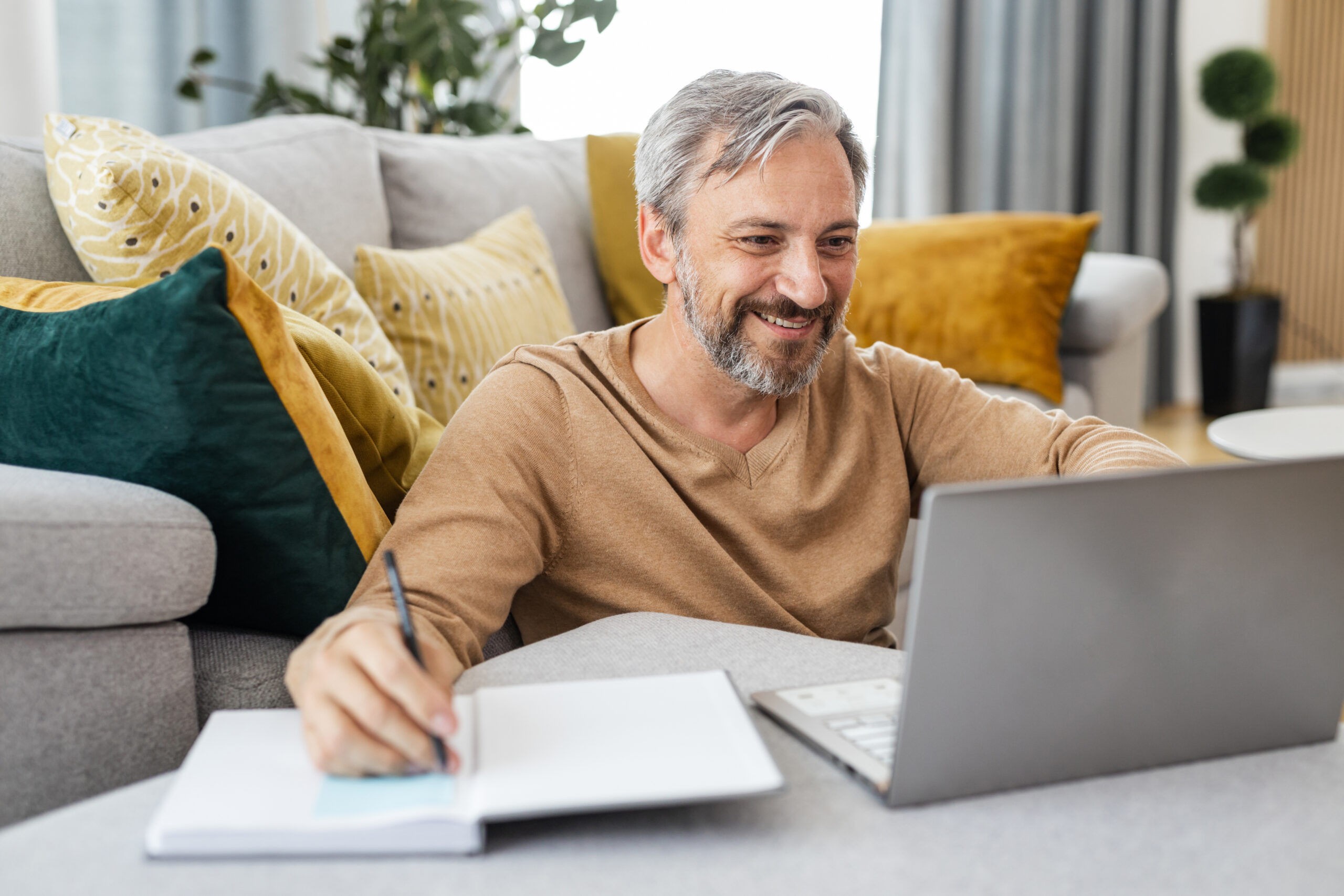 Man taking notes while watching laptop